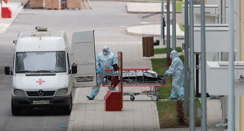 Медицинские специалисты в защитном снаряжении толкают носилки к машине скорой помощи. Фото REUTERS/Максим Шеметов Медицинские специалисты в защитном снаряжении толкают носилки к машине скорой помощи. Фото REUTERS/Максим Шеметов