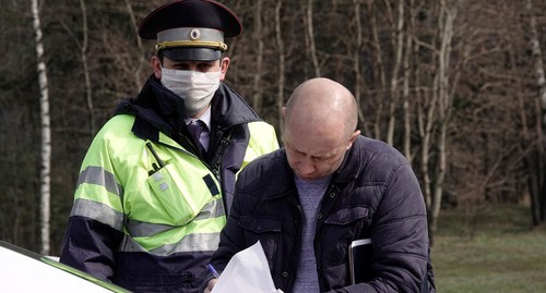 Мужчина заполняет документы рядом с сотрудником ГИБДД в защитной маске на контрольно-пропускном пункте. Фото REUTERS/Tatyana Makeyeva Мужчина заполняет документы рядом с сотрудником ГИБДД в защитной маске на контрольно-пропускном пункте. Фото REUTERS/Tatyana Makeyeva