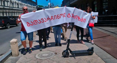 Участники акции проносят транспарант "спасем туризм" над электронным самокатом для аренды. Фото Беслана Кмузова для "Кавказского узла" Участники акции проносят транспарант "спасем туризм" над электронным самокатом для аренды. Фото Беслана Кмузова для "Кавказского узла"